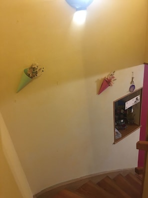 Una cantonada d'una habitació amb terra de fusta, un objecte de forma cònica verd i una petita estant amb diversos objectes.