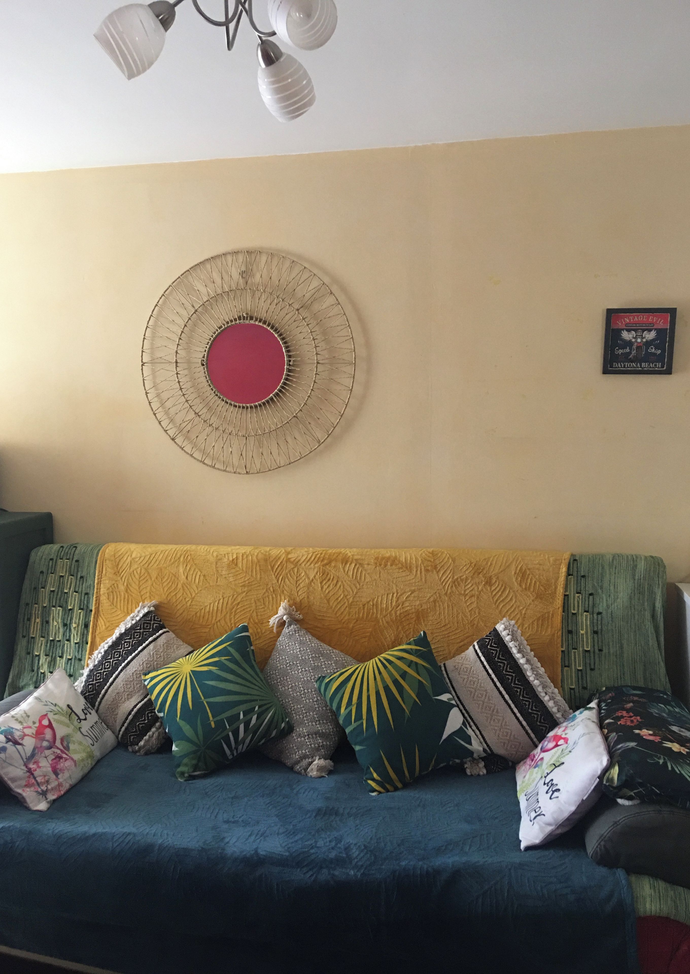 Een kamer met een bank, een decoratieve wandversiering en een plafondlamp.