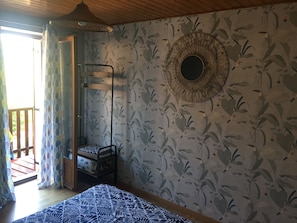 Una habitación con una cama, una lámpara colgante, un papel tapiz estampado y una ventana con cortinas.