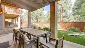 An outdoor patio with a wooden table and chairs, a covered seating area, and a fenced yard with trees. - Near Trails, Skiing & NAU! Family-Ready Home (Flagstaff)