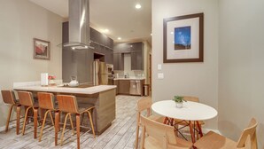 A modern kitchen with a central island, stainless steel appliances, and a dining area with wooden chairs and a white table. - Near Trails, Skiing & NAU! Family-Ready Home (Flagstaff)
