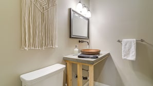 A bathroom with a toilet, a sink with a wooden countertop, a mirror with lights, and a macrame wall hanging. - Near Trails, Skiing & NAU! Family-Ready Home (Flagstaff)
