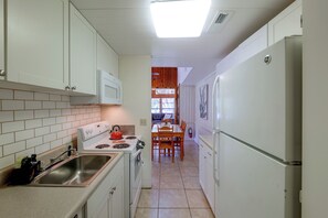 Une cuisine étroite avec des meubles blancs, une cuisinière, un évier et un réfrigérateur.