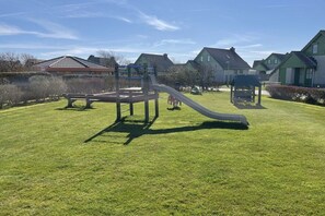 Un parc infantil amb tobogan i estructures d'escalada, envoltat de cases amb sostres verds.