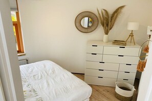 Un dormitori amb llit, una petarrera amb calaixos, un mirall i plantes decoratives.