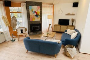 A living room with a fireplace, blue sofas, a television, and a painting on the wall. - Bungalow with 1 bedroom (Den Helder, Julianadorp)