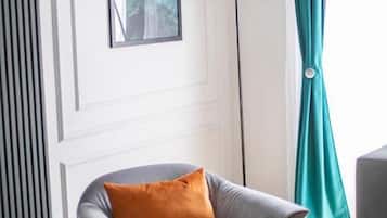 Una habitación moderna con un sillón gris, una lámpara de pie, un cuadro enmarcado en la pared y cortinas color esmeralda.