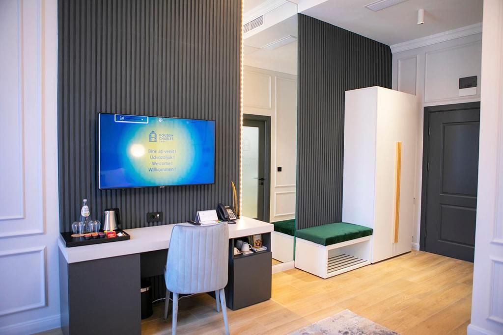 Een moderne hotelkamer met een flatscreen televisie, een bureau met stoel, een groene gestoffeerde bank en een garderobe.