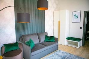 A modern living room with a grey sofa, green cushions, a blue rug, and a tall floor lamp.