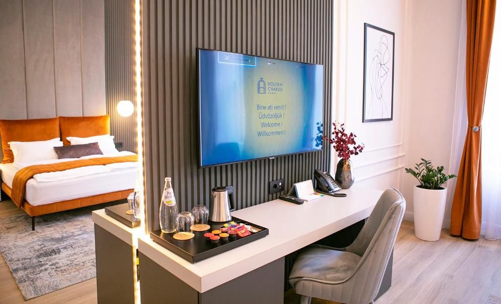 Een moderne hotelkamer met een bed, een bureau met een flatscreen televisie, een koffiezetapparaat en een vaas met bloemen.