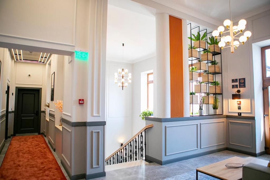 Een hotellobby met een trap, een receptiebalie met planten en een kroonluchter.
