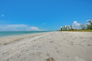 A wide sandy beach with clear turquoise water, a few scattered trees, and a distant building. - Secluded Island Escape on Little Gasparilla Island (Placida)