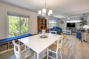 A spacious living area with a dining table, seating, a television, and a large window offering a view of greenery. - Secluded Island Escape on Little Gasparilla Island (Placida)