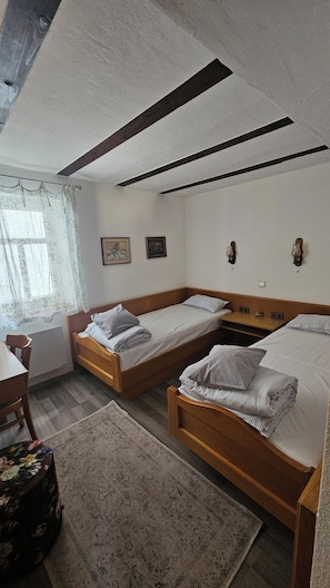 Una habitación con dos camas de madera, un escritorio, una silla y una ventana con cortinas.