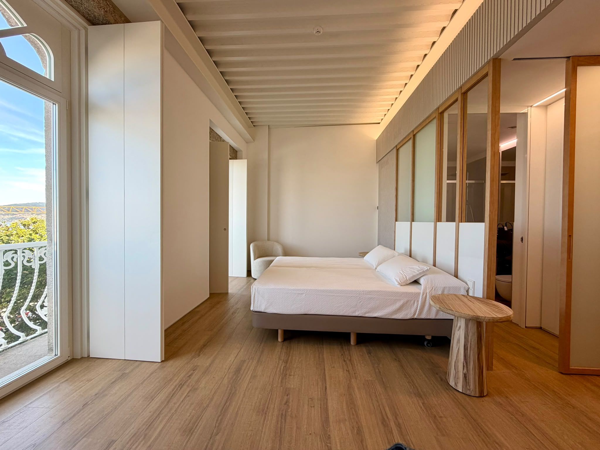 A modern bedroom with a bed, a small table, and a view of the outdoors.