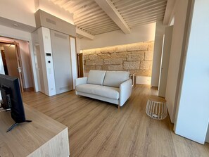 A modern living room with a sofa, a television, and a stone wall. - Cíes Suitel Mar e Vía (Vigo)