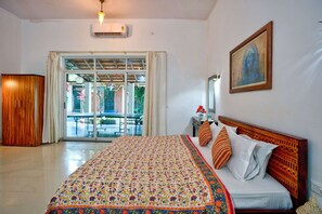 A hotel room with a large bed, a wooden wardrobe, a balcony with a view, and a painting on the wall. - Lux Beachfront 2 BHK Private Pool Villa in Morjim | 100mtr to Beach (Morjim)
