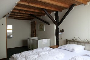 Ein Schlafzimmer mit Holzboden, einem Babybett, einem Bett und einem Nachttisch.