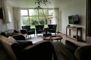 Ein Wohnzimmer mit einer Couch, zwei Sesseln, einem Couchtisch und einem an der Wand befestigten Fernseher.