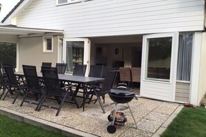 Eine Terrasse im Freien mit Esstisch und Stühlen, einem Grill und einer überdachten Sitzgruppe.