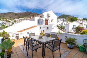 A terrace with a table and chairs, surrounded by potted plants and a decorative wall. - Villa in Nerja With Private Pool & Jacuzzi (Nerja)