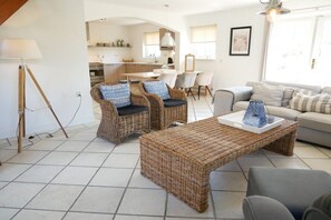 A living room with wicker furniture, a sofa, and a dining area with a table and chairs. - Holiday home with 3 bedrooms (Callantsoog)