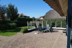 Un patio exterior con suelo de ladrillo, una mesa con sillas y una estructura de techo de paja.