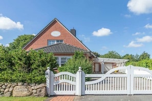 A red brick house with a white gate and a stone wall with a sign. - Holiday home with 3 bedrooms (Langenhorn)