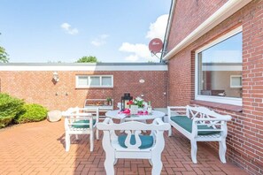 A patio with white furniture, a round table, and a brick wall. - Holiday home with 3 bedrooms (Langenhorn)