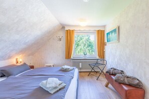 A bedroom with a bed, a bench, a radiator, and a window with curtains. - Holiday home with 3 bedrooms (Langenhorn)