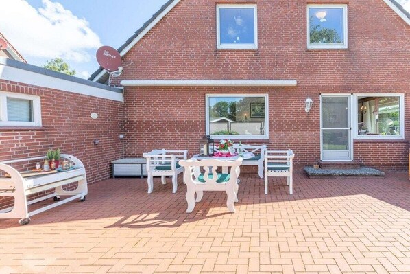 A brick house with a patio area featuring a table and chairs, a bench, and a satellite dish. - Holiday home with 3 bedrooms (Langenhorn)