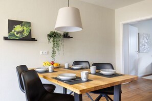 A dining area with a wooden table, black chairs, and a hanging light fixture. - Holiday apartment in Büsum with swimming pool (Büsum)