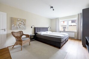Un dormitori amb un llit, fallegueres, una cadira, un quadre i una finestra.