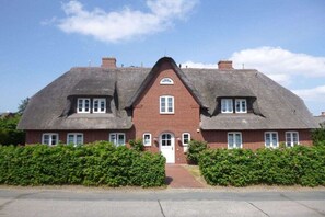 Een tweelaags huis met een symmetrisch ontwerp, met een centrale ingang, een puntige kap en een bakstenen gevel.
