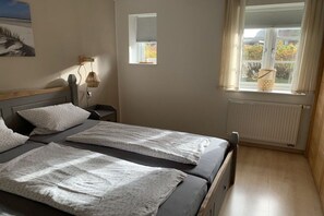 A bedroom with two beds, a nightstand, a wall-mounted lamp, a window with a view, and a radiator. - Holiday apartment in Nebel with swimming pool (Nebel)