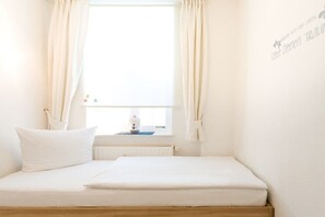 Ein schlicht eingerichtetes Schlafzimmer mit einem Bett, einem Fenster mit Vorhängen, einem Heizkörper und einer Wand mit einer Dekoration.