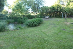 A grassy outdoor area with a small pond, dense shrubbery, and a table with chairs. - Country holiday at Birkenhof (Kittlitz)
