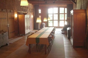 Ein langer Esstisch mit Stühlen, Holzboden und ein großes Fenster mit Vorhängen.