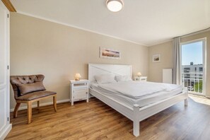 Ein Schlafzimmer mit einem Bett, einem Sessel, Nachttischen und einem Fenster.
