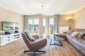 Un salon moderne avec un canapé, un fauteuil et un téléviseur à écran plat posé sur une console blanche.
