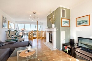 A modern living room with a fireplace, a television, and a dining area with chairs and a table. - Holiday apartment in Binz with swimming pool (Binz)