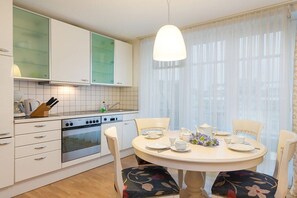 Una cucina con mobili bianchi, un fornello e un tavolo da pranzo per quattro persone con sedie decorate con motivi floreali.