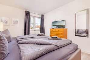 Ein Hotelzimmer mit einem Bett, einem Fernseher, einem Schminktisch und einem Fenster mit Vorhängen.