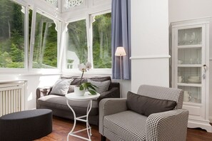A room with a view of greenery, a sofa, a chair, a small table with a plant, and a cabinet with glassware. - Sea jewel in Villa Agnes (Binz)