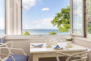A dining area with a table set for two, a window with a view of the sea, and a chair with a blue cushion. - Sea jewel in Villa Agnes (Binz)