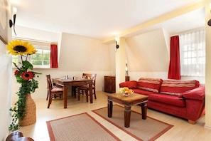 A living room with a dining table, red sofa, and a vase with flowers. - Amber in the Villa Lucky (Binz)