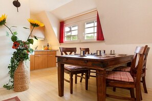 A dining area with a wooden table and chairs, a vase with flowers, and a window with curtains. - Amber in the Villa Lucky (Binz)