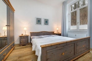 A bedroom with a wooden bed, bedside tables with lamps, a radiator, and two framed pictures on the wall. - Sea greetings at Villa Agnes (Binz)
