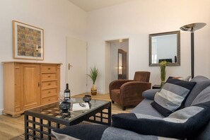 A living room with a sofa, armchair, coffee table, wooden cabinet, and a mirror on the wall. - Sea greetings at Villa Agnes (Binz)