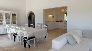 A spacious dining area with a white table and chairs, a white sofa, and a kitchen with white cabinets. - Maison Olivette: Provençal villa with a private pool, 6 bedrooms, and olive trees (Flayosc)